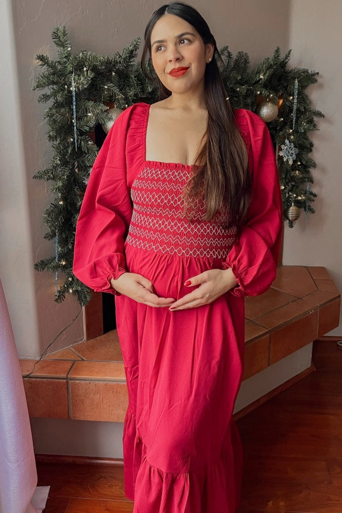 woman wearing a bright pink maternity maxi dress with smocked bodice and puff sleeves, holding her baby bump