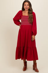 woman wearing a red maternity dress with puff sleeves and smocked bodice, standing against a neutral background