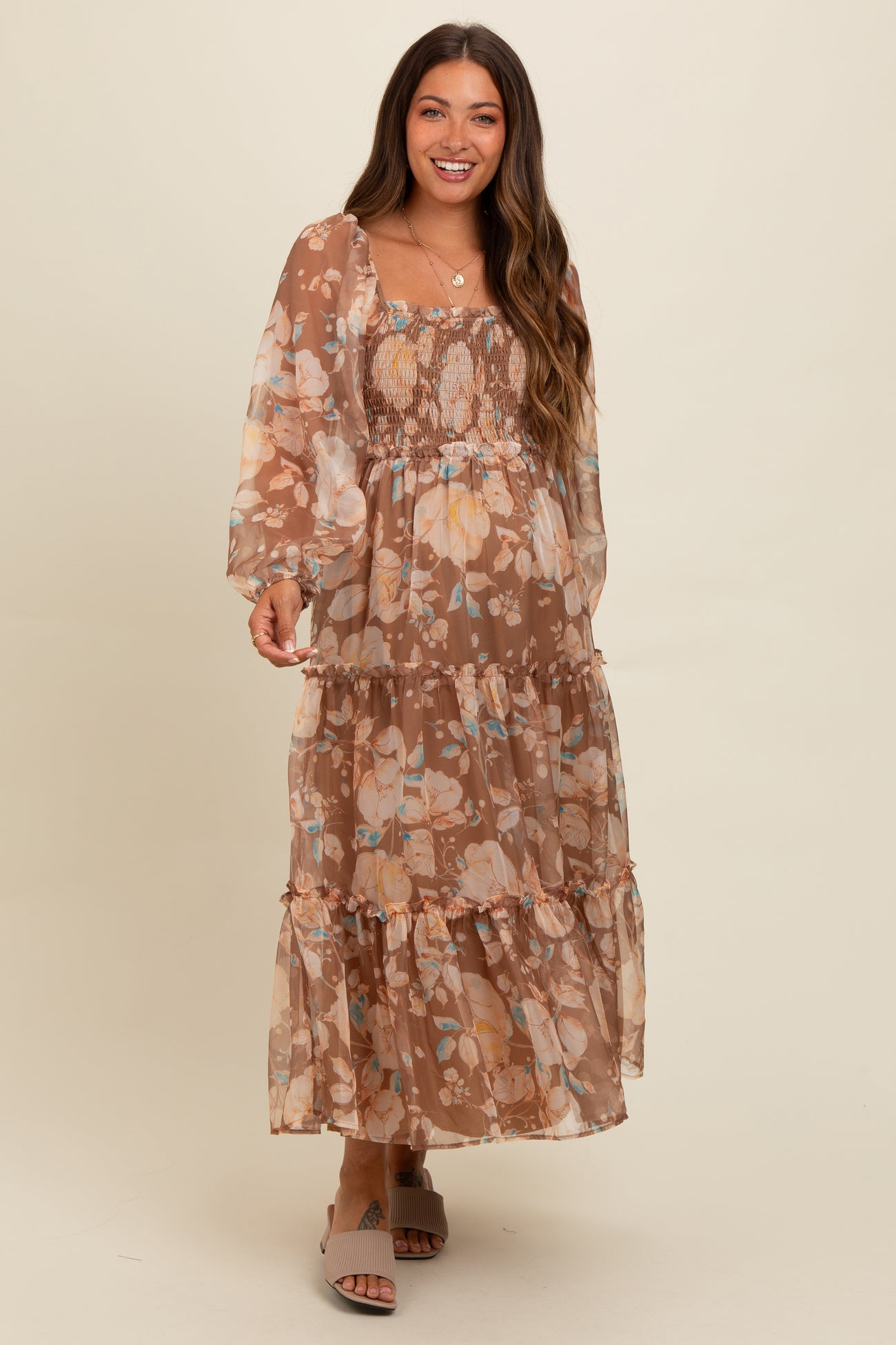 woman wearing a brown floral maternity maxi dress with long sleeves and a smocked bodice, displaying her baby bump