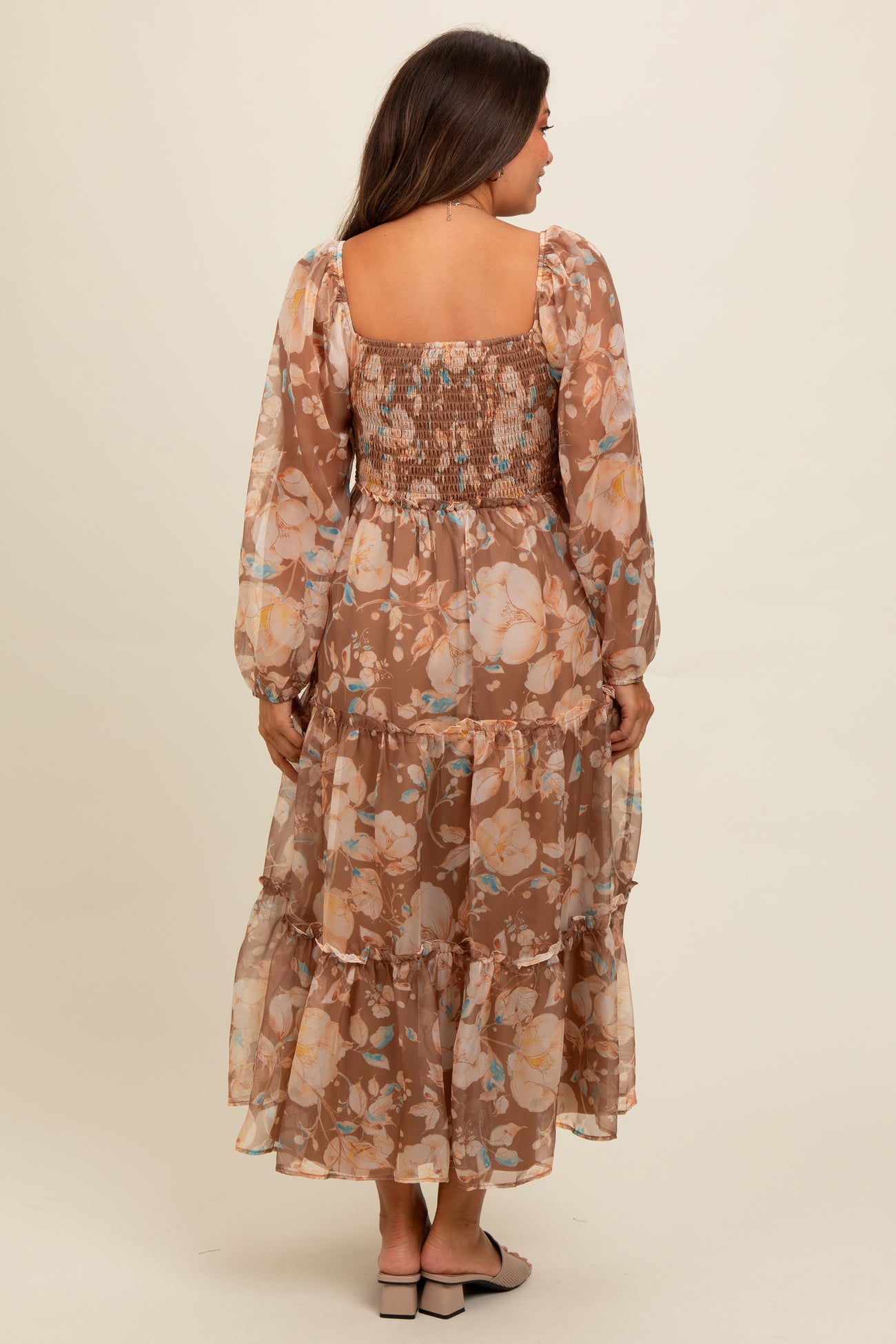 woman wearing a brown floral maternity dress with long sleeves and a flowy tiered skirt, showcasing the back view