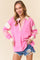 woman wearing a pink long sleeve pullover with striped collar and sleeves, paired with distressed denim shorts