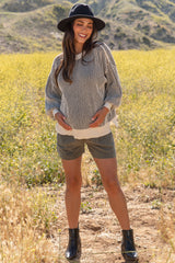 woman wearing a striped maternity sweater and shorts, holding her baby bump in a scenic outdoor setting