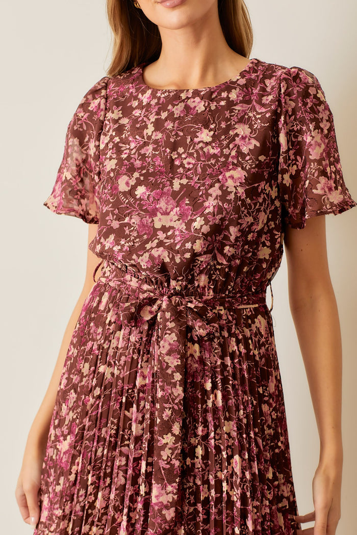 woman wearing a brown floral pleated dress with short puff sleeves and a belted waist