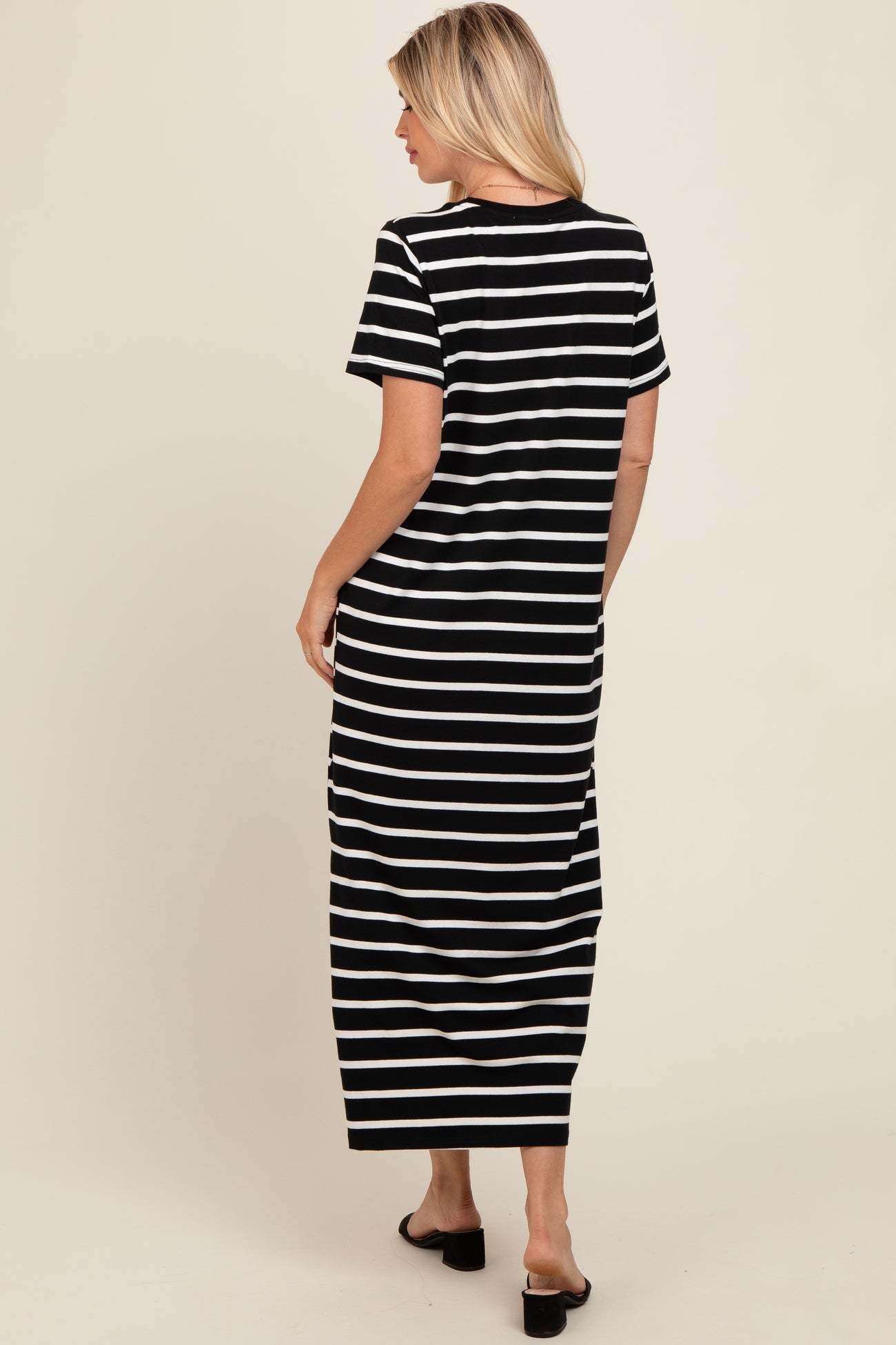 woman wearing a black and white striped maxi dress with short sleeves, standing with her back to the camera