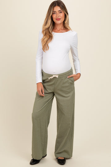 woman wearing a white long sleeve maternity top and green checkered wide-leg maternity pants with a visible baby bump