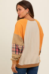 woman wearing a color-blocked maternity sweatshirt in mustard and beige with plaid sleeves