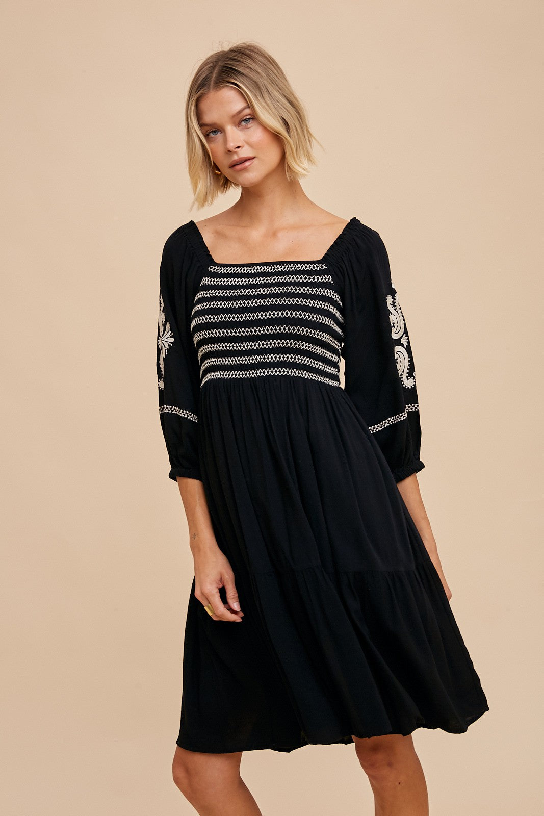 woman wearing a black embroidered dress with a square neckline and three-quarter sleeves