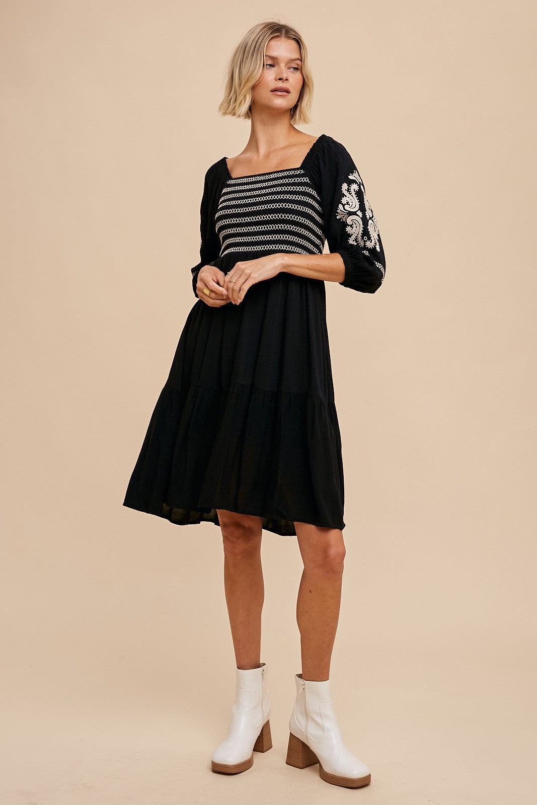 woman wearing a black tiered dress with embroidered details and three-quarter puff sleeves, paired with brown ankle boots