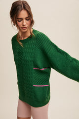 woman wearing a green oversized cable knit sweater with pink stripe accents and long sleeves