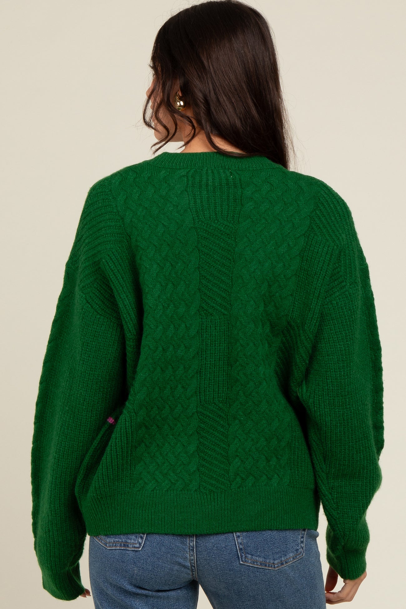 woman wearing a chunky green cable-knit sweater with a relaxed fit, viewed from the back