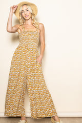 woman wearing a floral print strapless jumpsuit in mustard yellow with pockets and straw hat