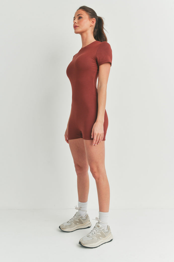 woman wearing a rust-colored short sleeve bodysuit with a fitted style and athletic shoes