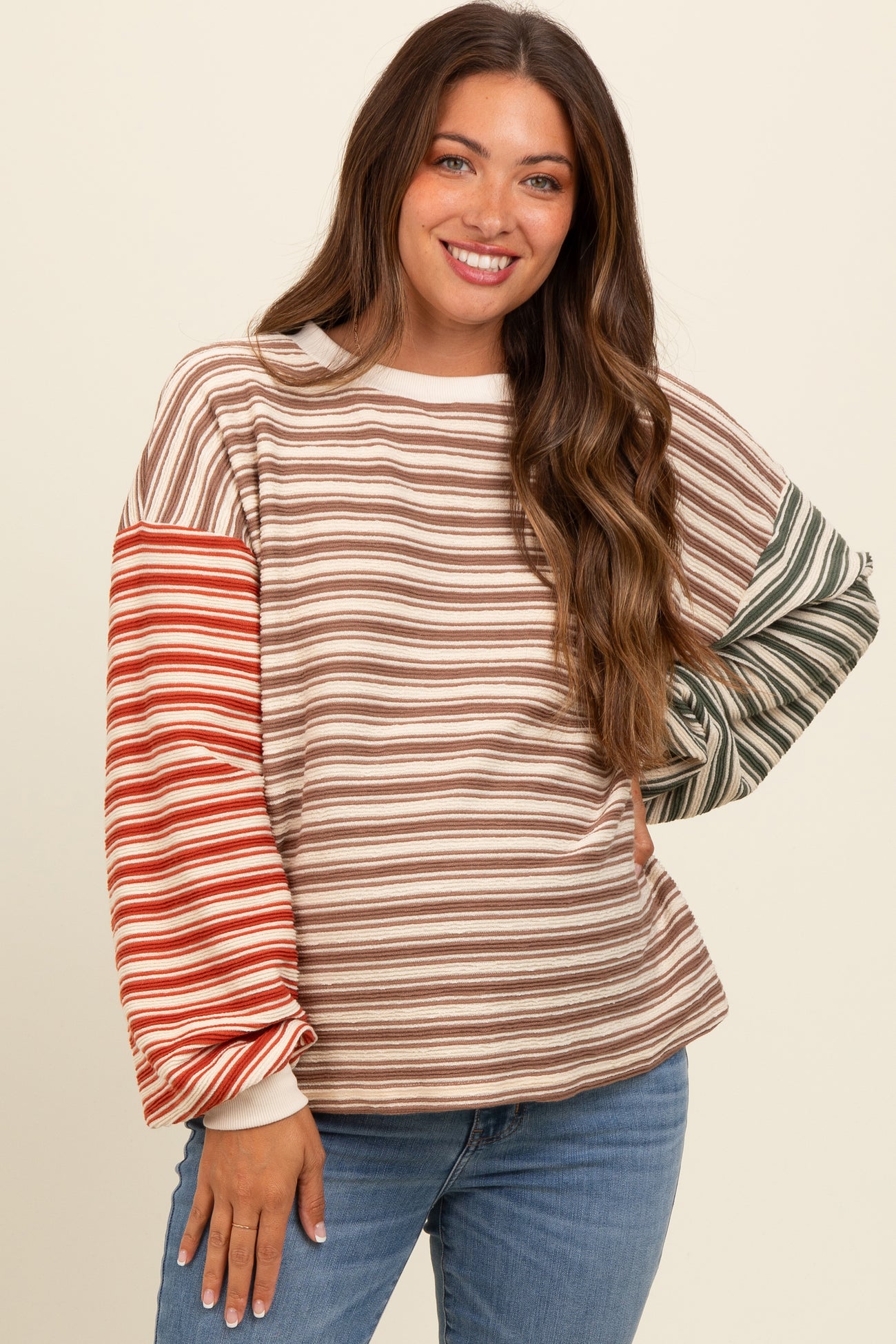 woman wearing a striped maternity sweatshirt with long sleeves in earthy tones and smiling at the camera