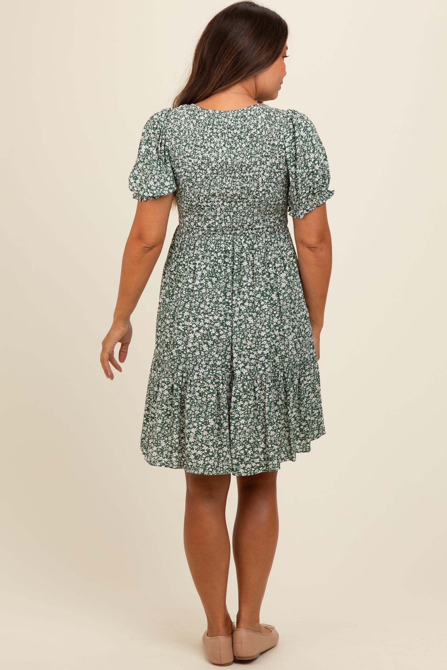 woman wearing a green floral maternity dress with short sleeves and a flared skirt, showing a relaxed fit from the back