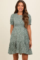 woman wearing a green floral maternity dress with short puff sleeves and a tiered skirt, smiling at the camera