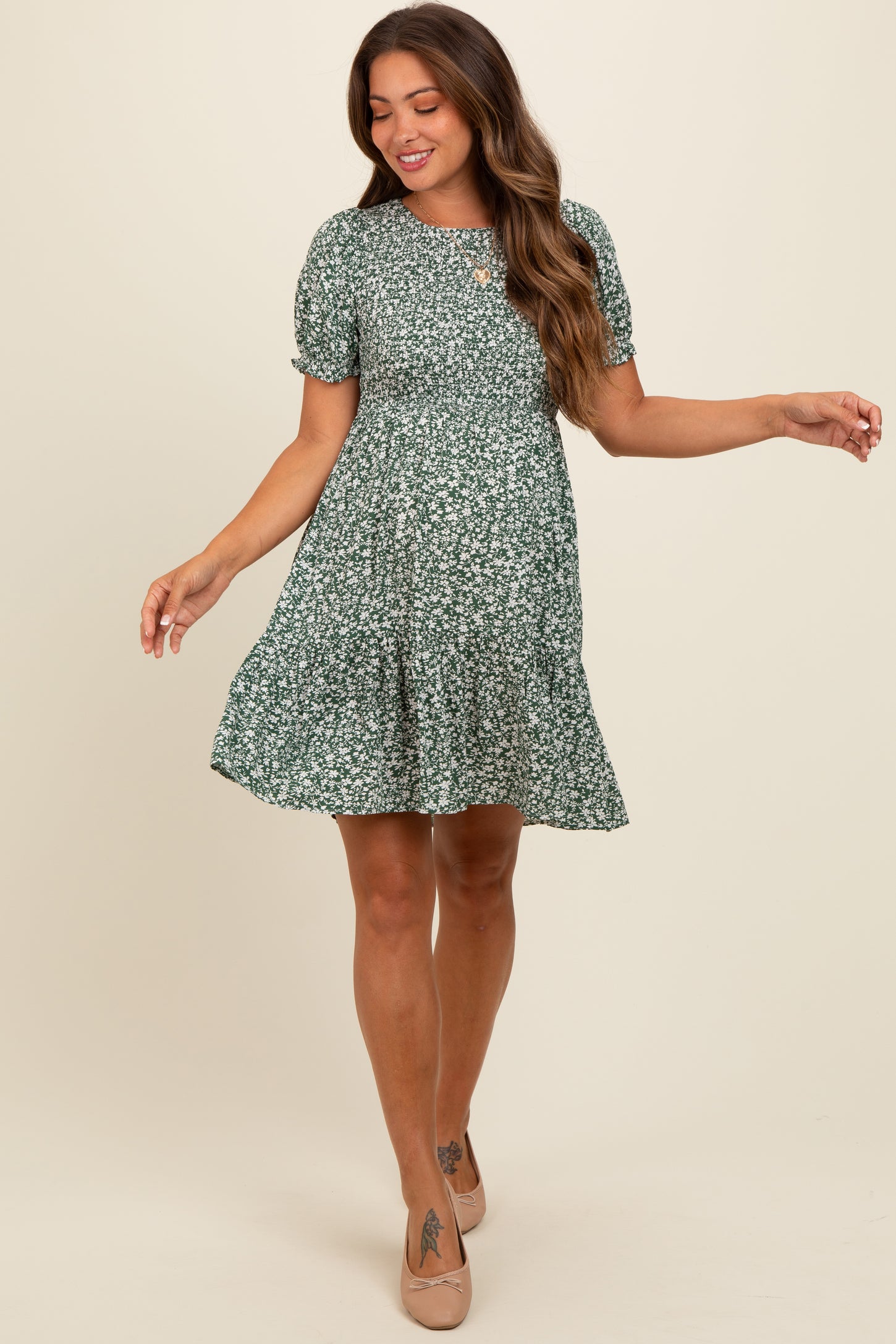 woman wearing a green floral maternity dress with short puff sleeves and a tiered skirt, showcasing a baby bump