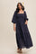 woman wearing a navy blue square neck maxi dress with puff sleeves and eyelet detailing, standing with one hand in a pocket