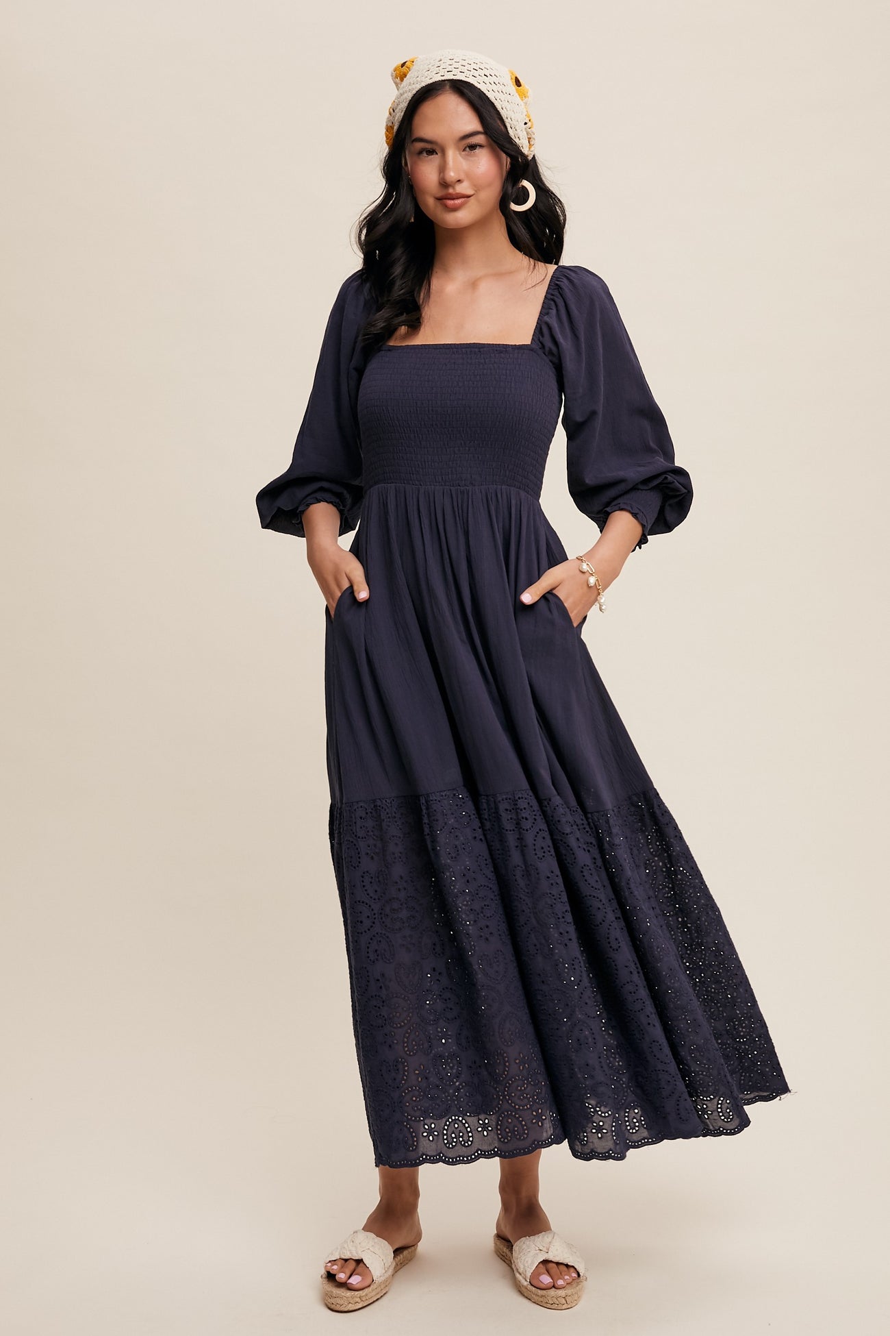 woman wearing a navy blue maxi dress with a smocked bodice, puff sleeves, and lace detailing at the hem