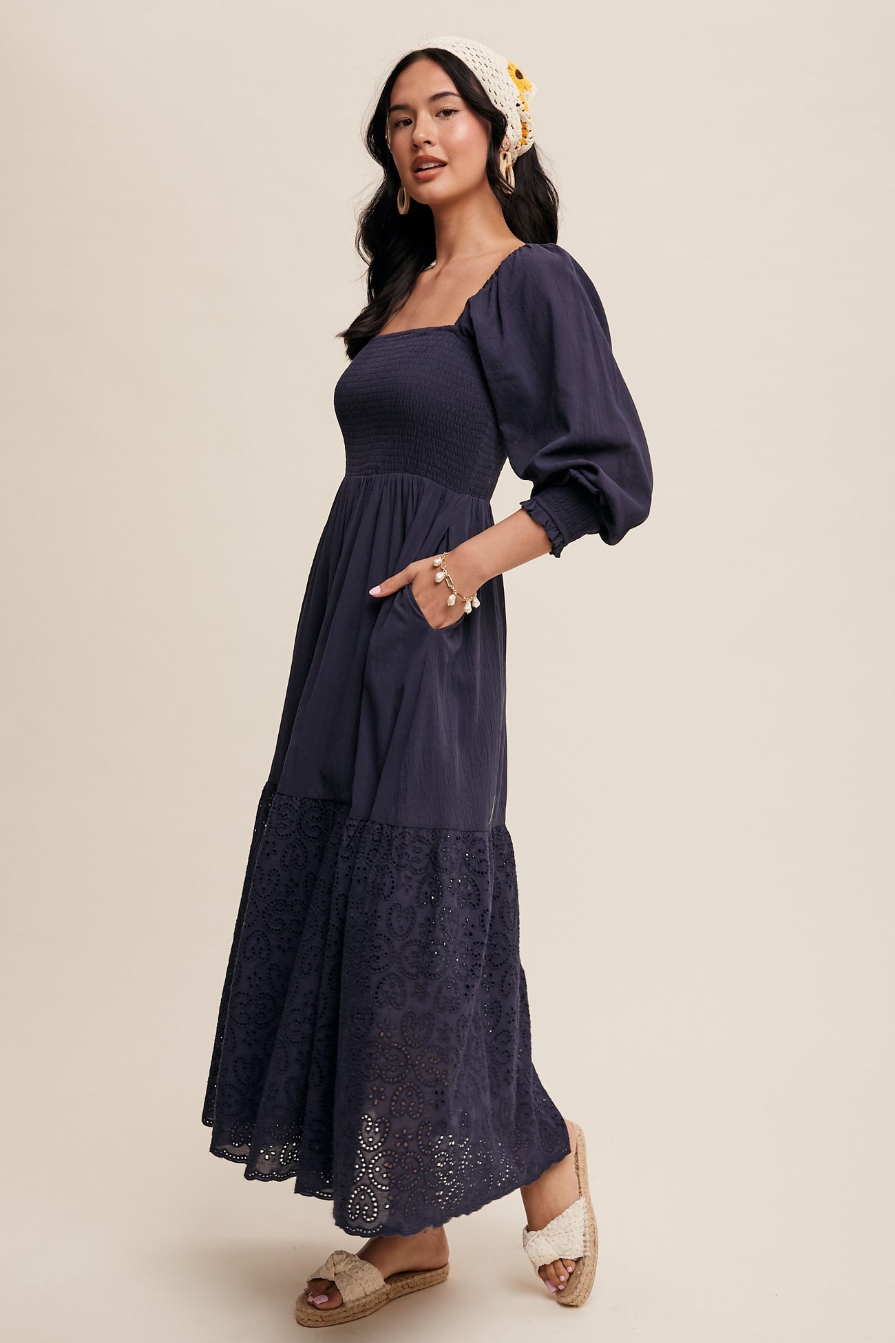 woman wearing a navy blue smocked maxi dress with puff sleeves and lace detailing, posing in a side view