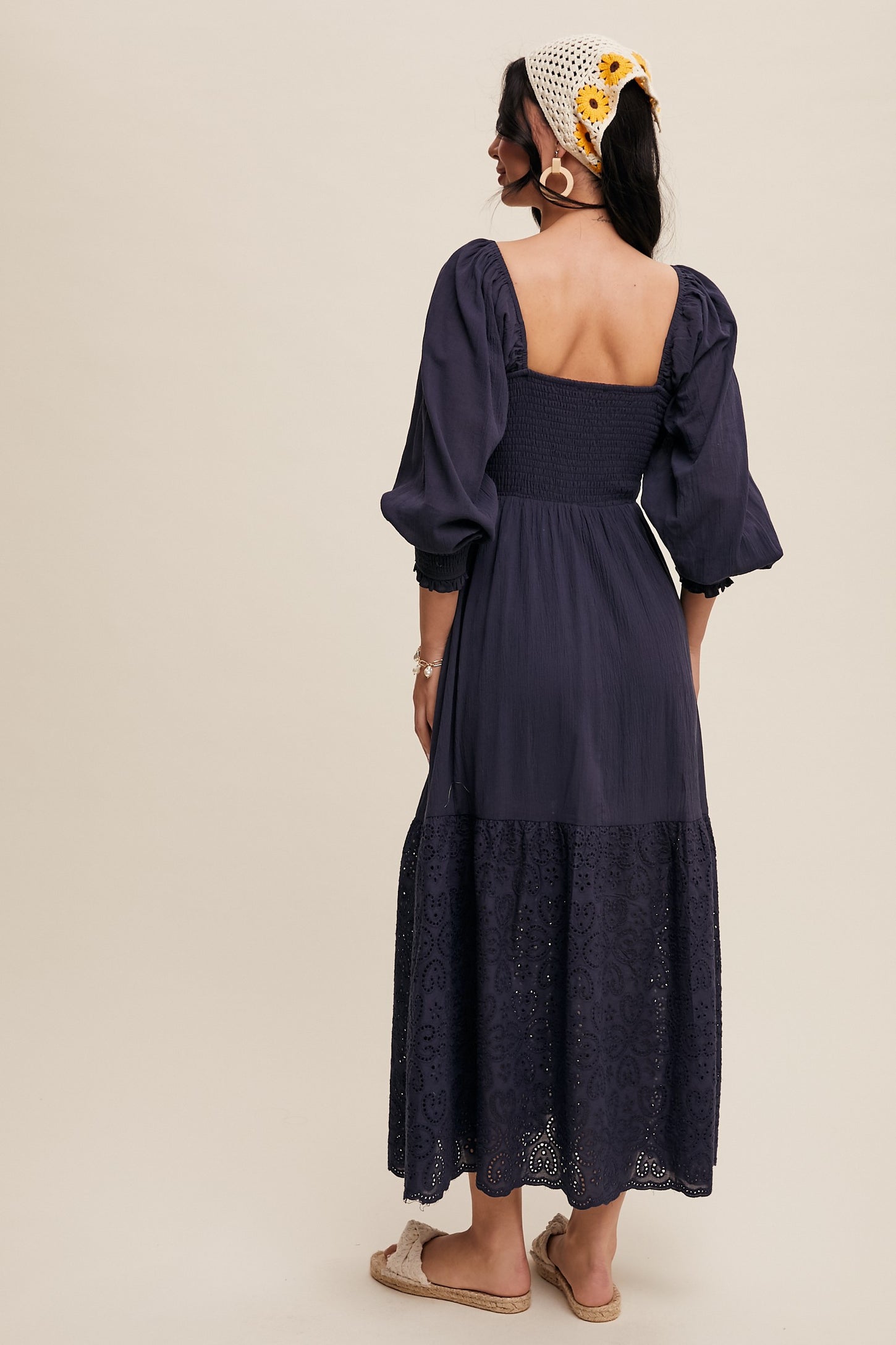 woman wearing a navy blue puff sleeve maxi dress with a smocked bodice and lace trim at the hem, viewed from the back