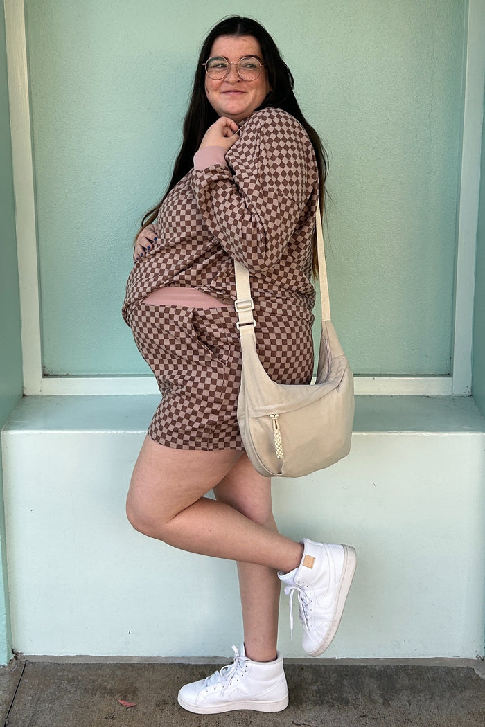 woman wearing a brown checkered maternity short set with a visible baby bump and holding a beige shoulder bag