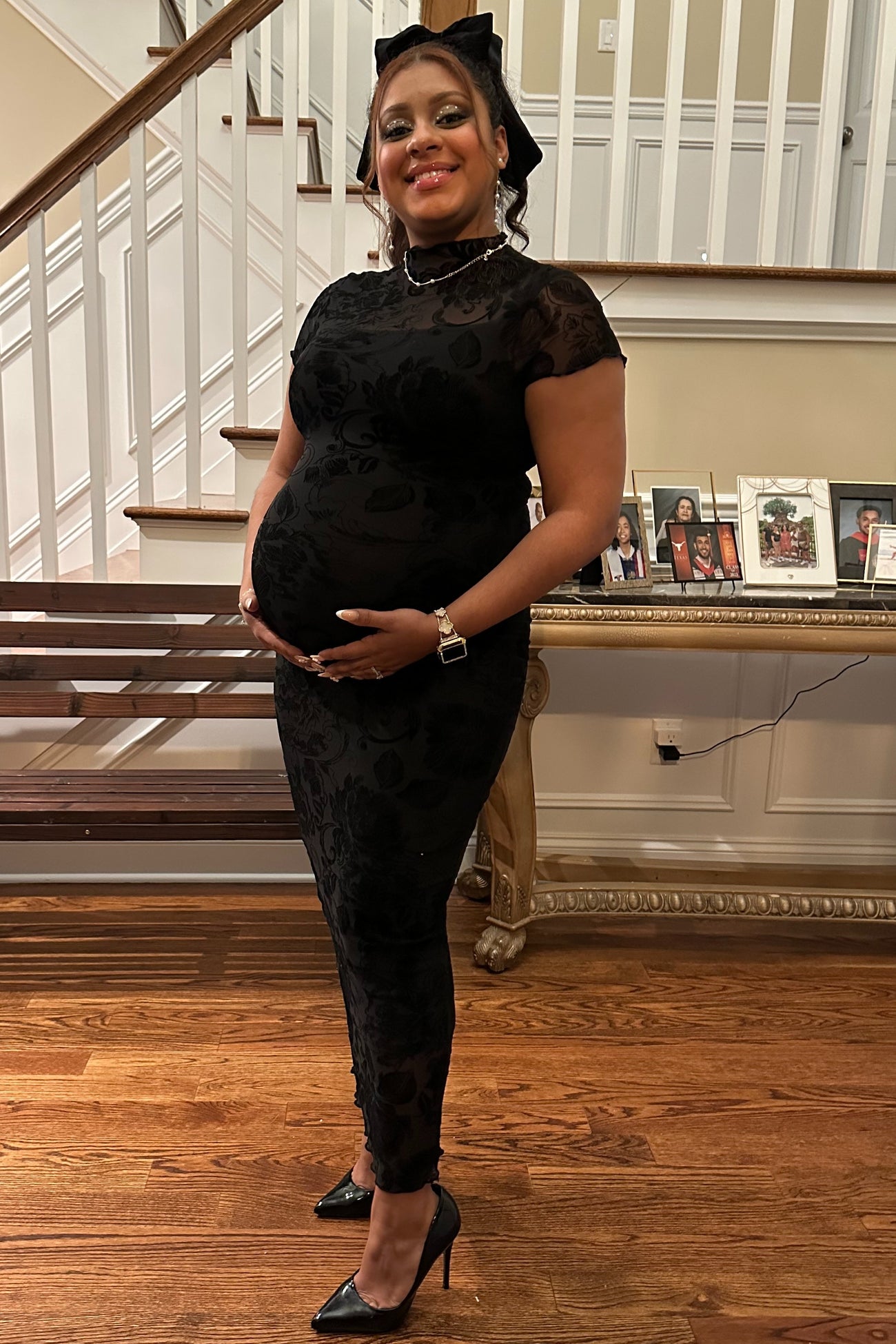 woman wearing a black lace maternity dress and holding her baby bump while standing on a staircase