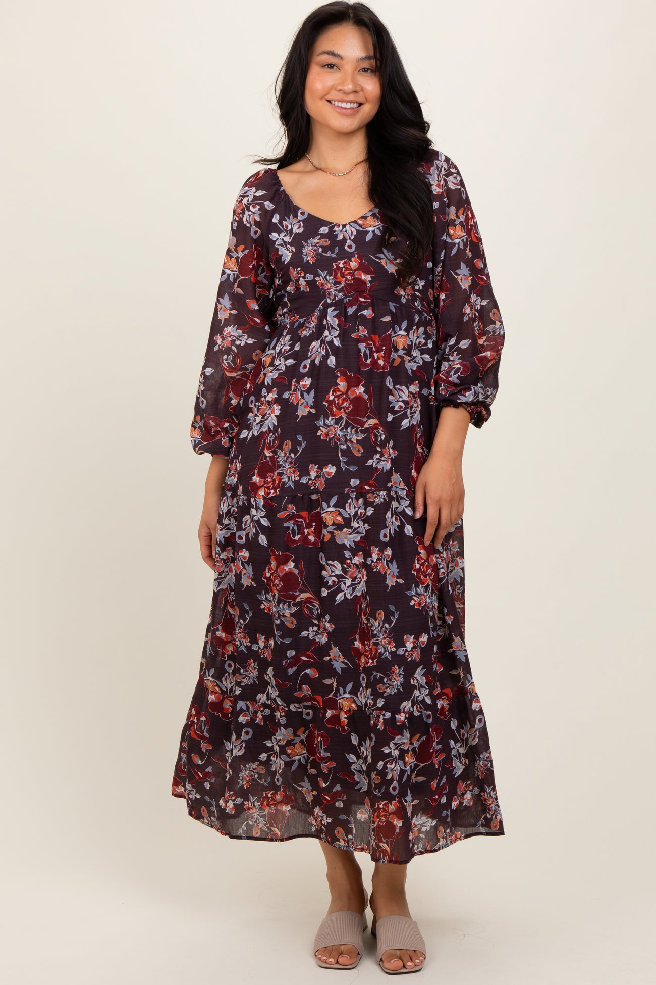 woman wearing a dark floral maxi dress with long sleeves and a ruffled hem, smiling at the camera