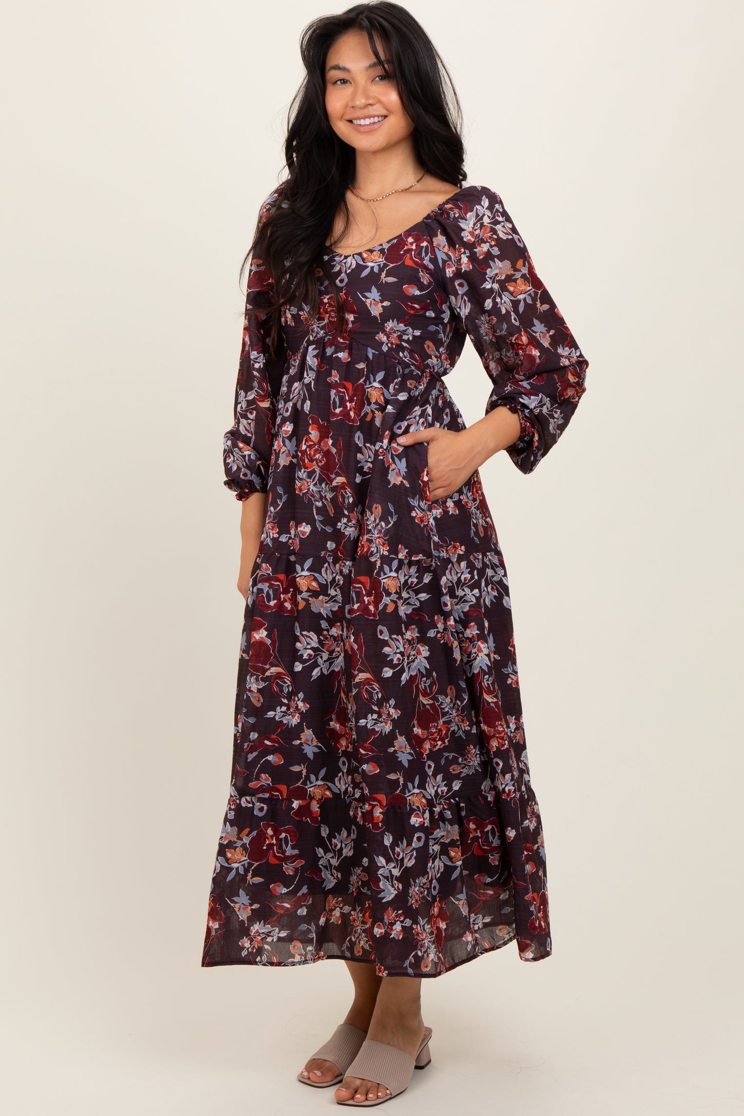 woman wearing a dark floral maxi dress with three-quarter sleeves and pockets, standing and smiling