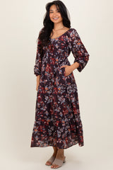 woman wearing a dark floral maxi dress with three-quarter sleeves and pockets, standing and smiling