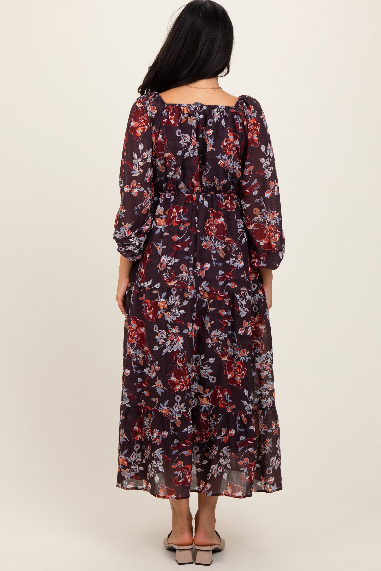 woman wearing a dark floral maxi dress with long sleeves and a cinched waist, viewed from the back