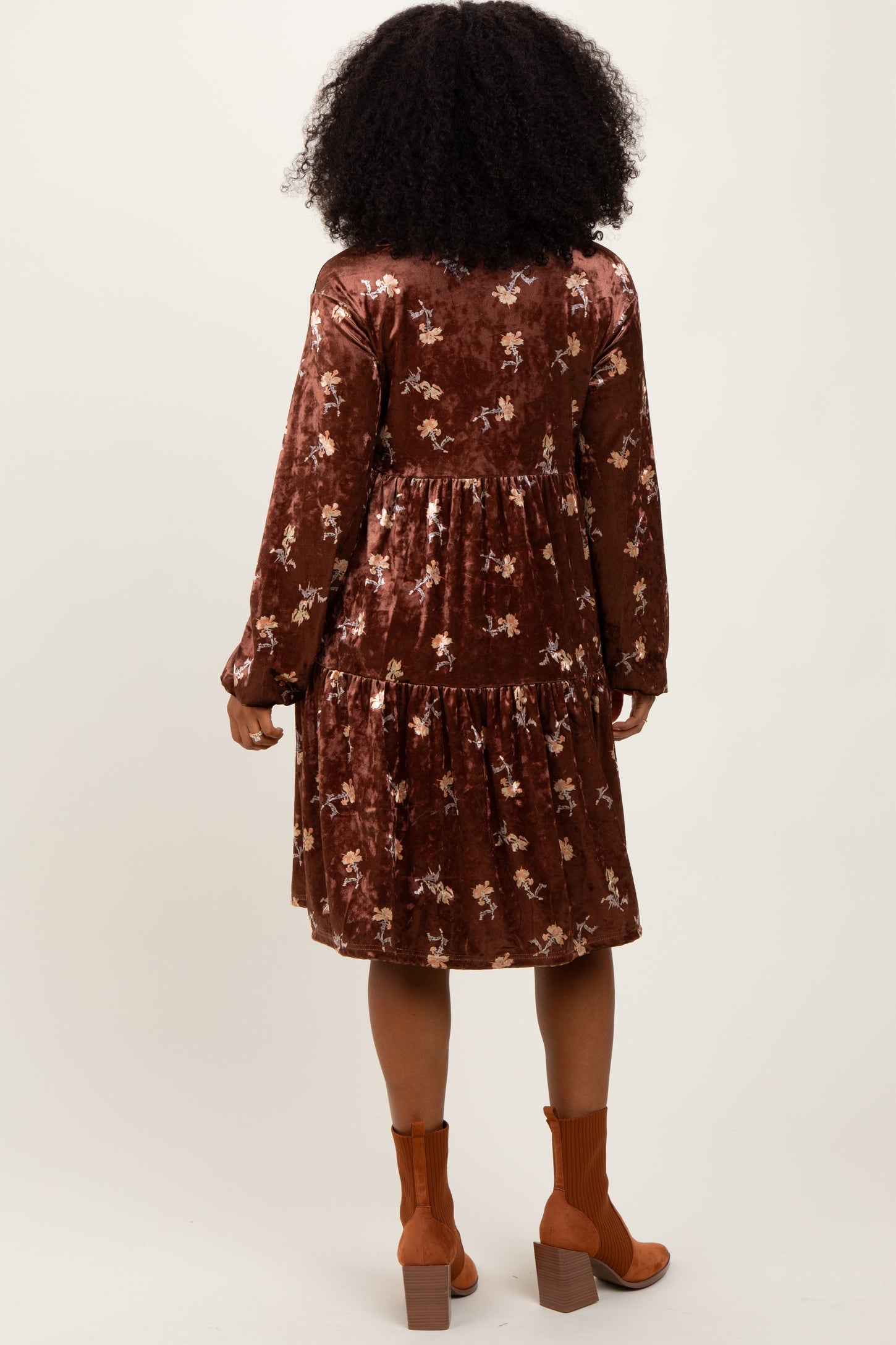 woman wearing a brown floral velvet dress with long sleeves and a tiered skirt, viewed from the back