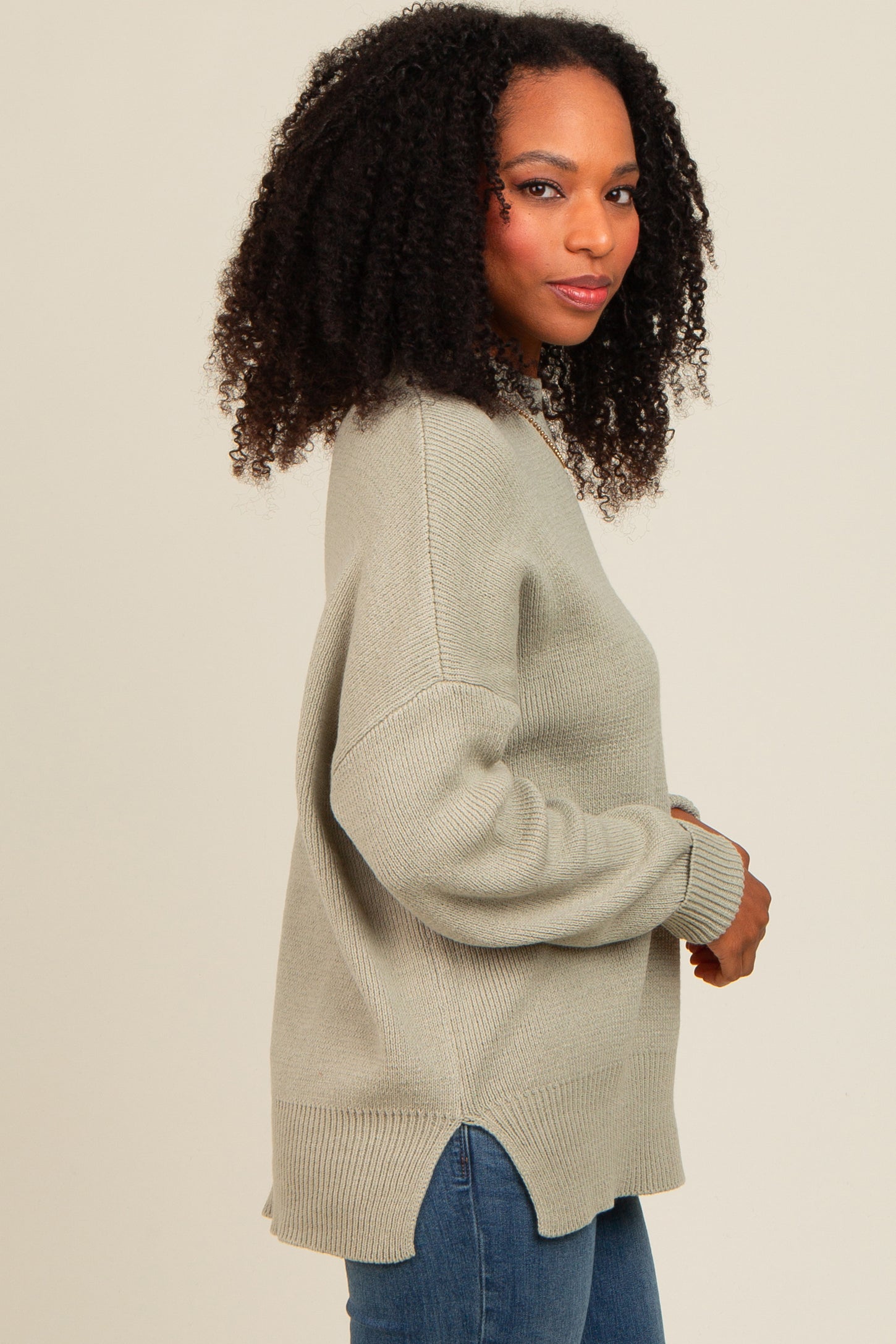 woman wearing a light green oversized sweater with side slits and medium wash jeans