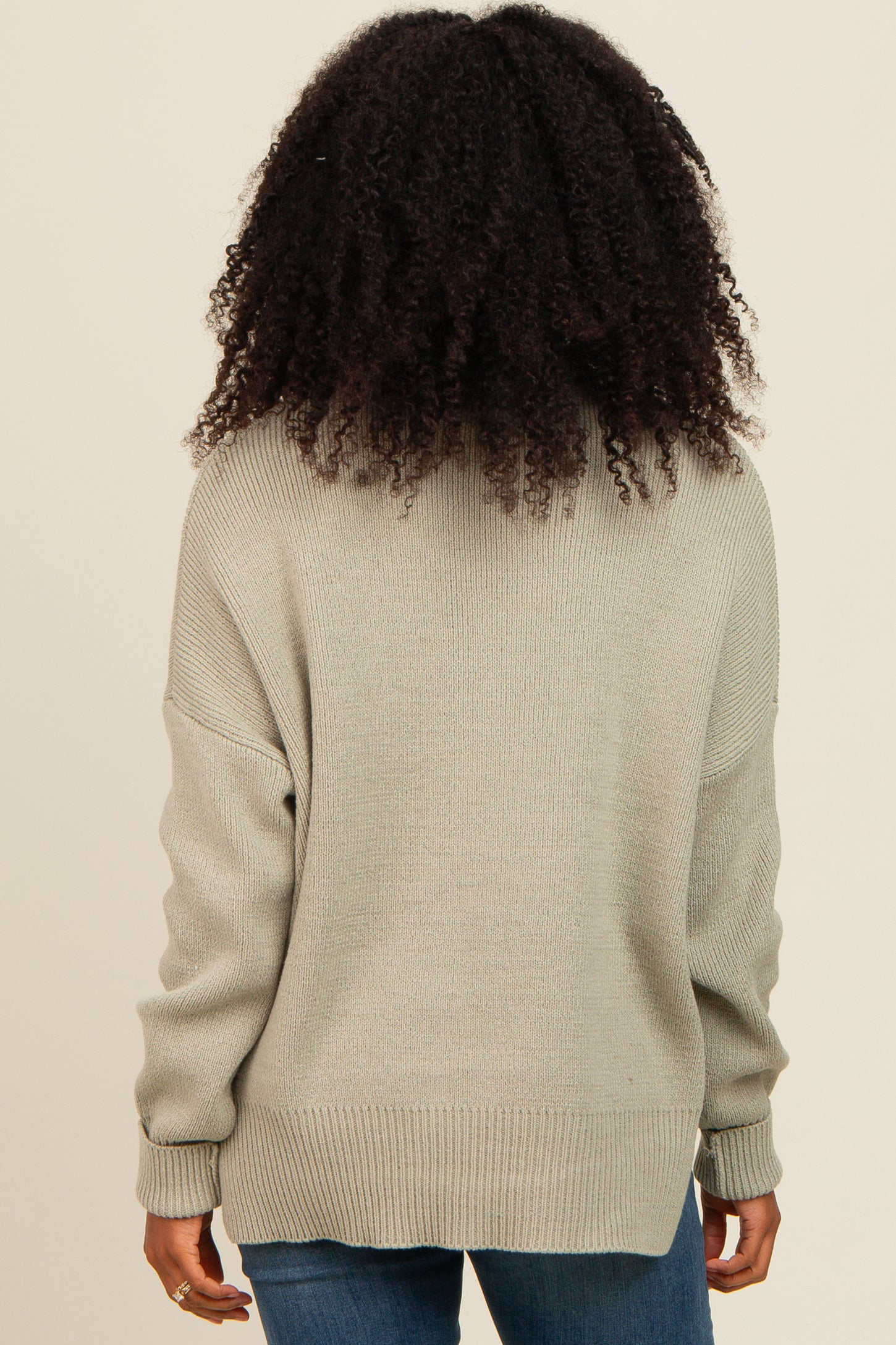 woman wearing a light gray oversized sweater with a crew neckline and ribbed details, viewed from the back