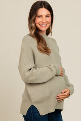 woman wearing a light green oversized maternity sweater and holding her baby bump