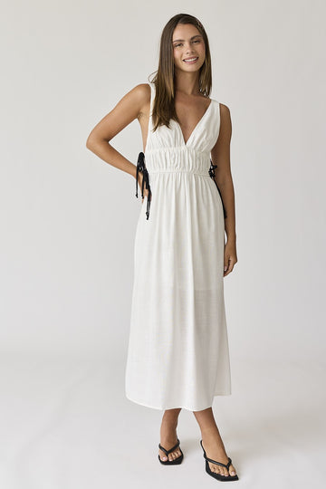 woman wearing a white long maxi dress with adjustable tie straps and a v-neckline, styled with black flip-flops