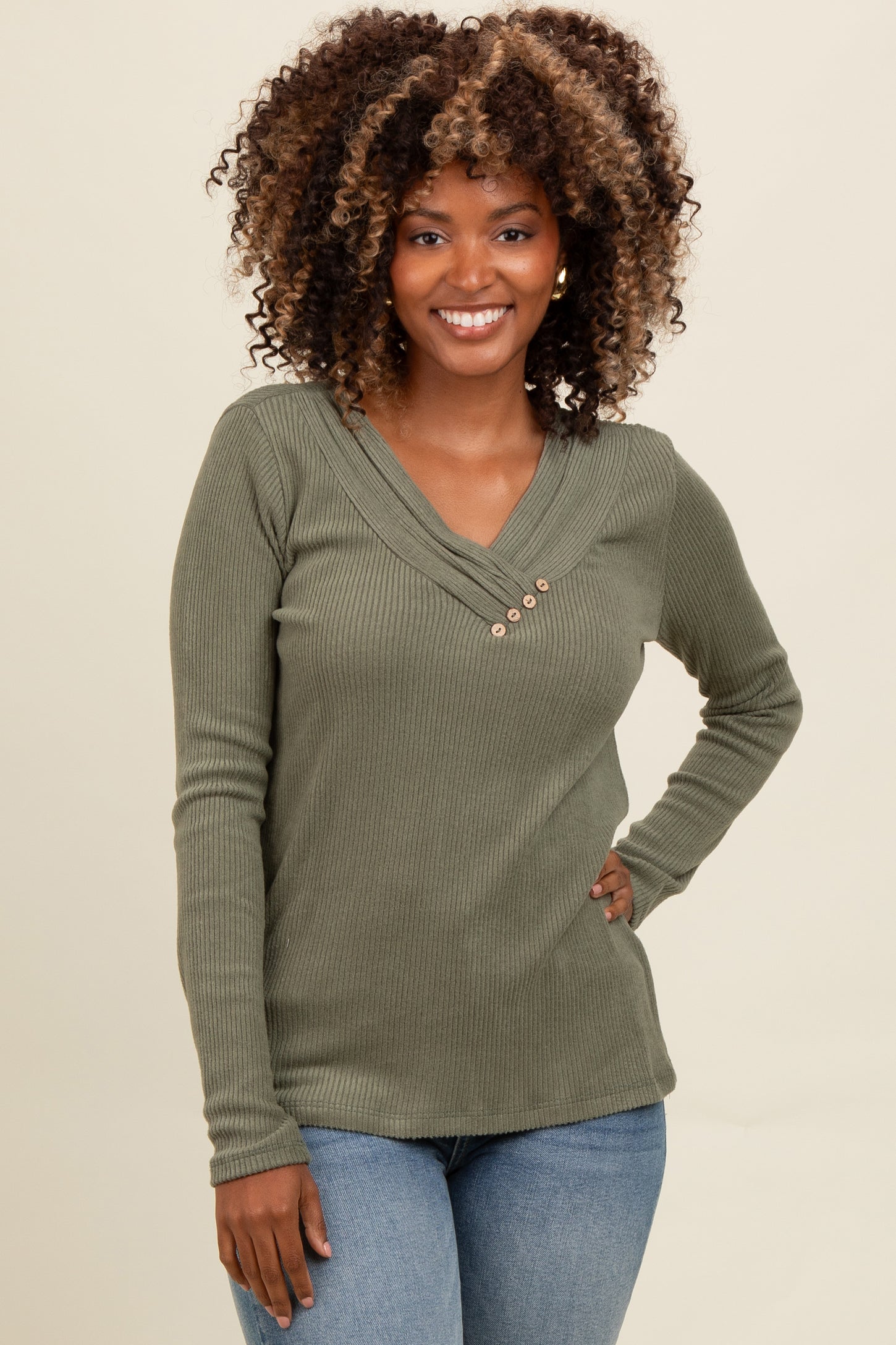 woman wearing a green ribbed long sleeve top with a v-neck and button details, smiling at the camera
