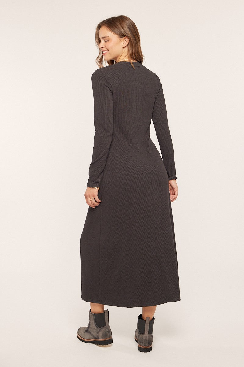 woman wearing a long sleeve dark gray maxi dress with a fitted silhouette and ankle boots, viewed from the back