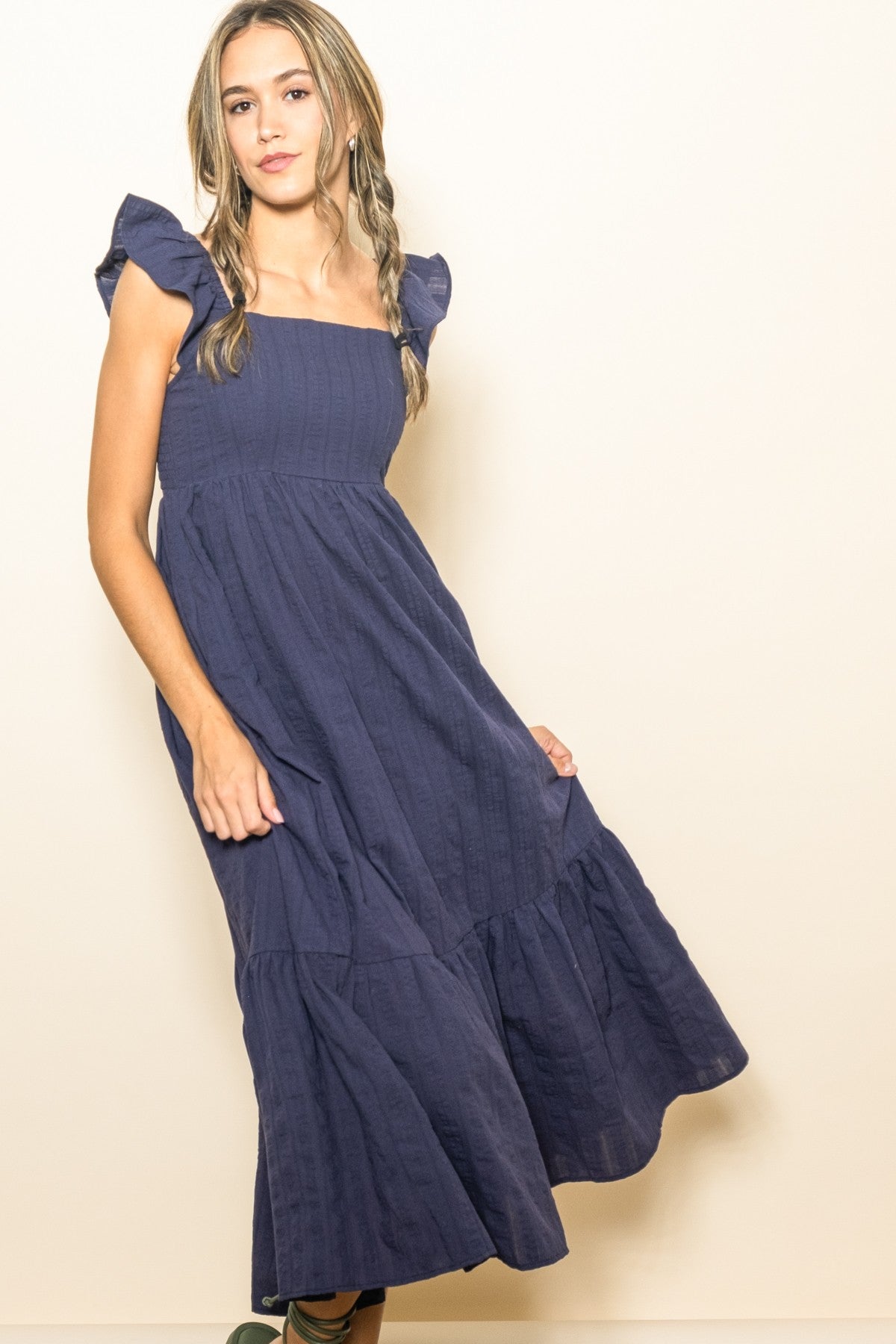 woman wearing a navy blue off-shoulder maxi dress with ruffled sleeves and a tiered skirt