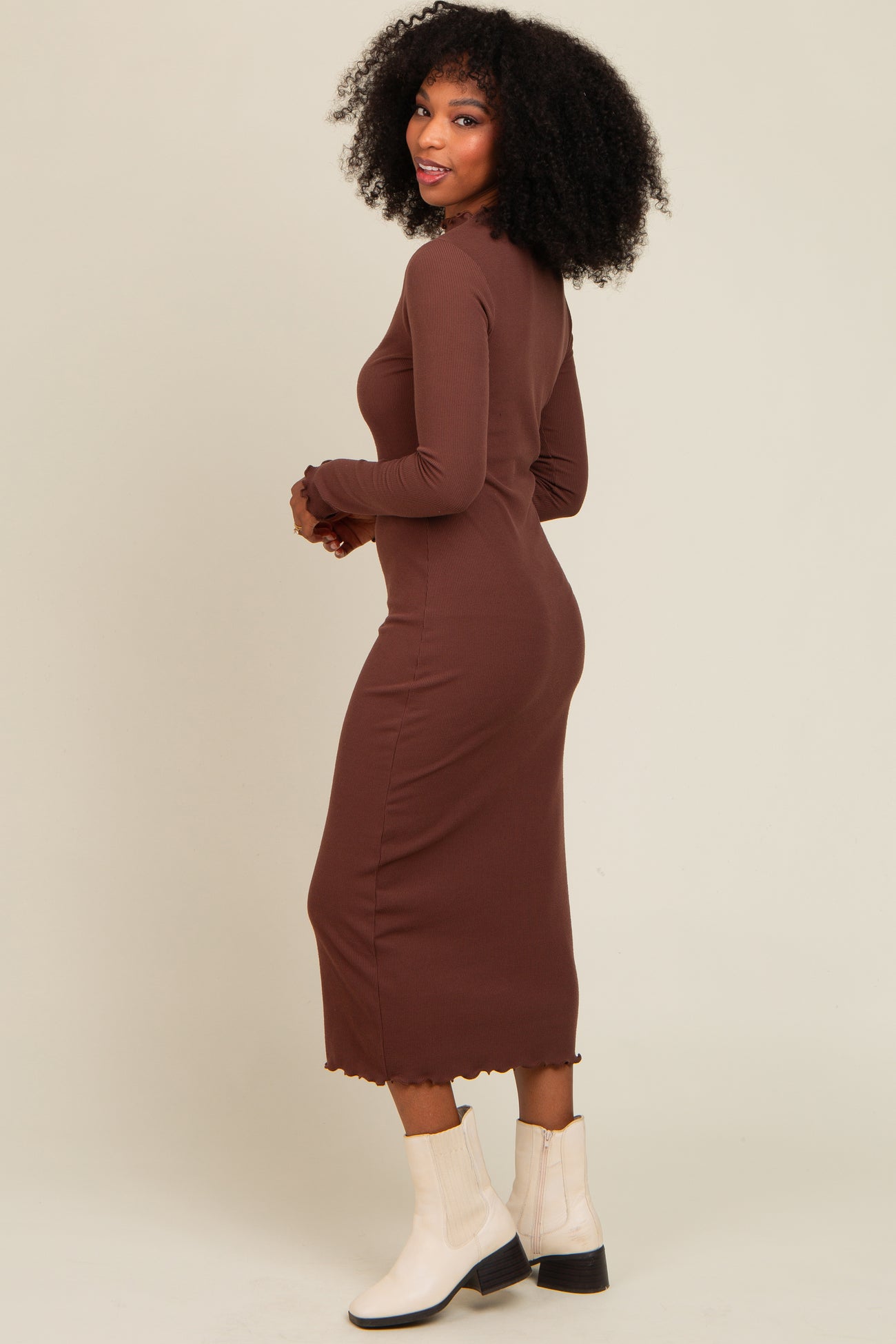 woman wearing a brown long sleeve ribbed midi dress with a scalloped hem and paired with white ankle boots