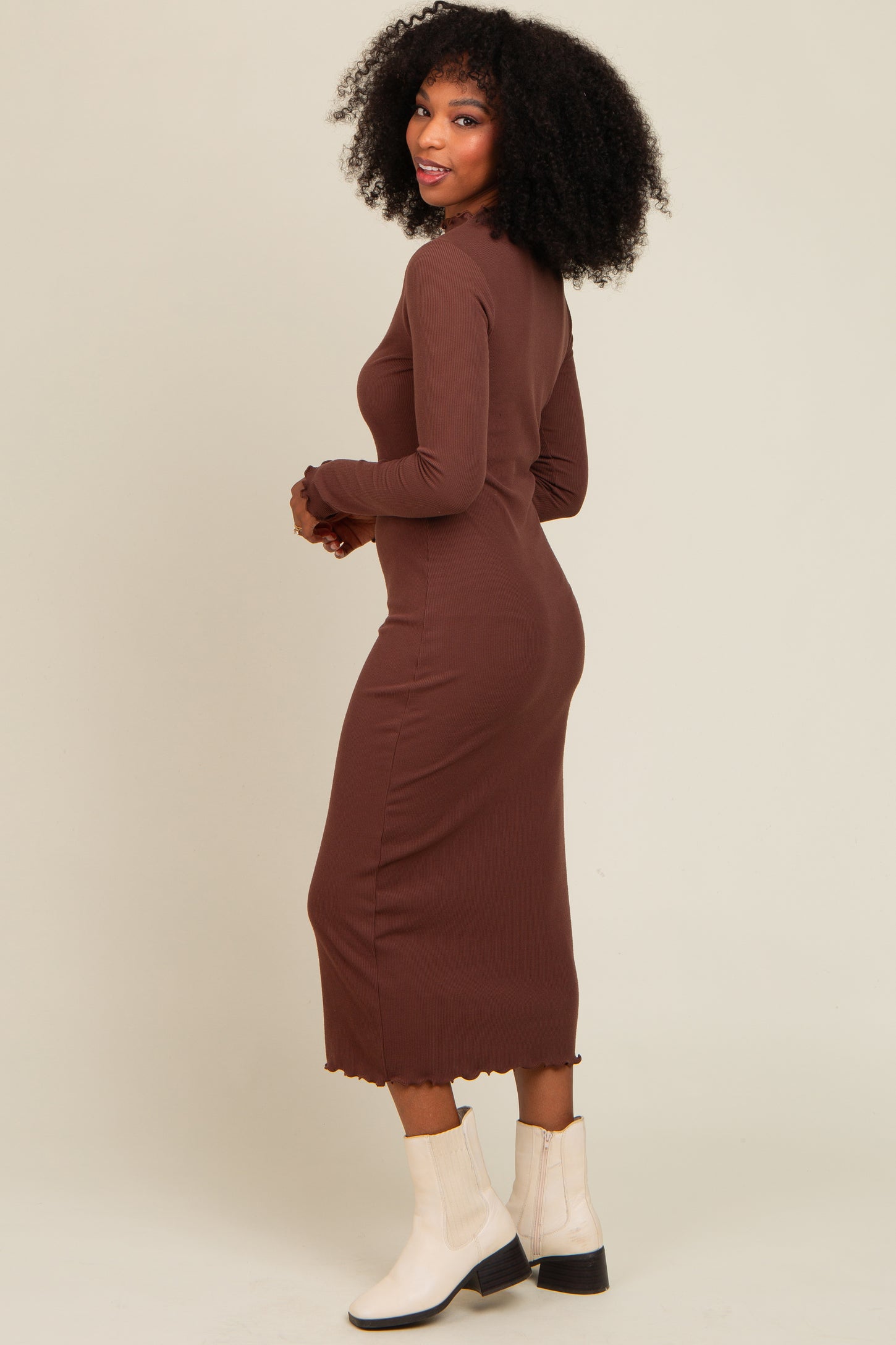 woman wearing a brown long sleeve ribbed midi dress with a scalloped hem and paired with white ankle boots