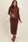 woman wearing a brown ribbed maternity dress with a scalloped neckline and long sleeves, holding her baby bump