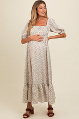 woman wearing a cream floral maternity dress with short puff sleeves and a tiered maxi skirt, holding her baby bump