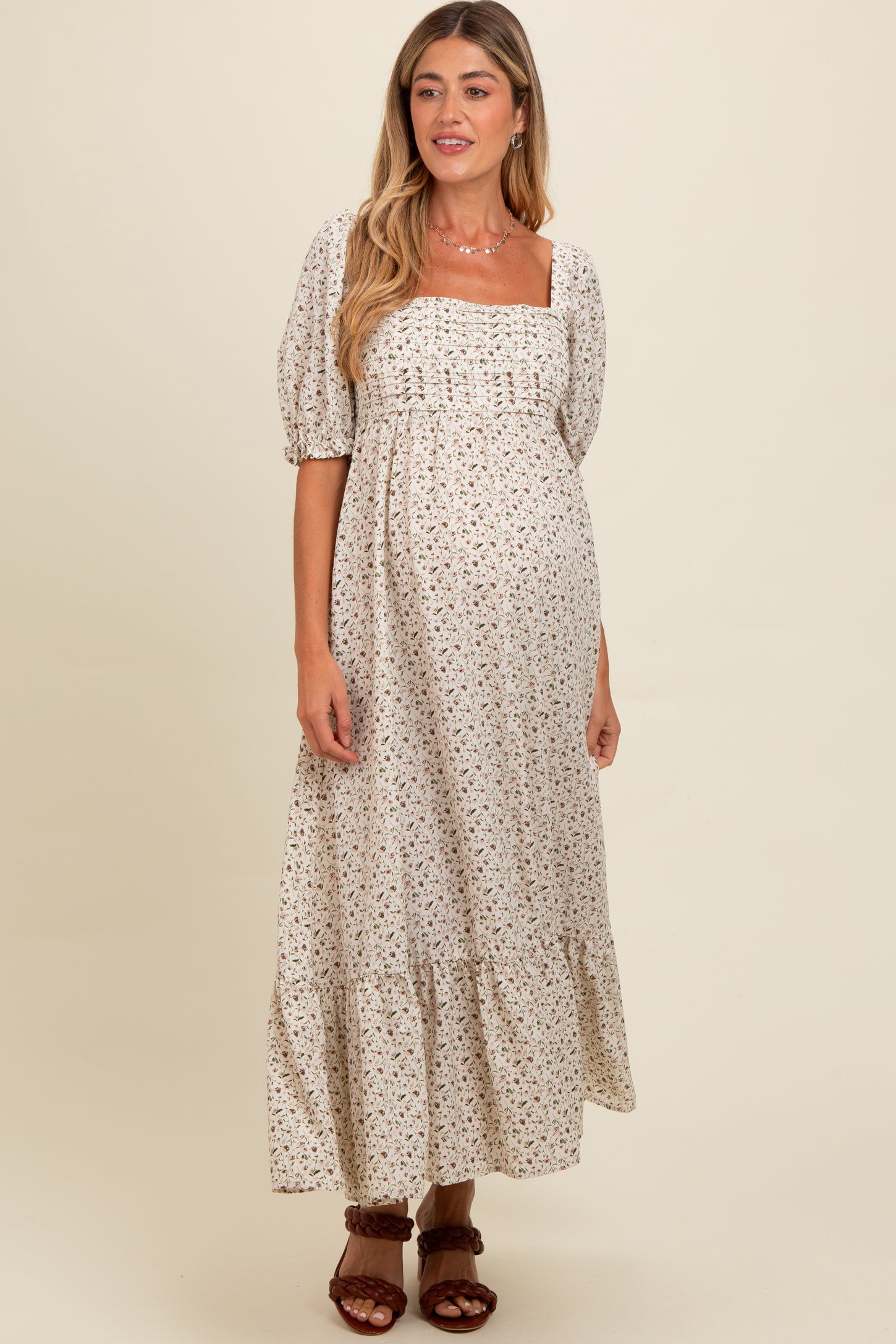 woman wearing a cream floral maternity maxi dress with puff sleeves and a tiered hem, showing her baby bump