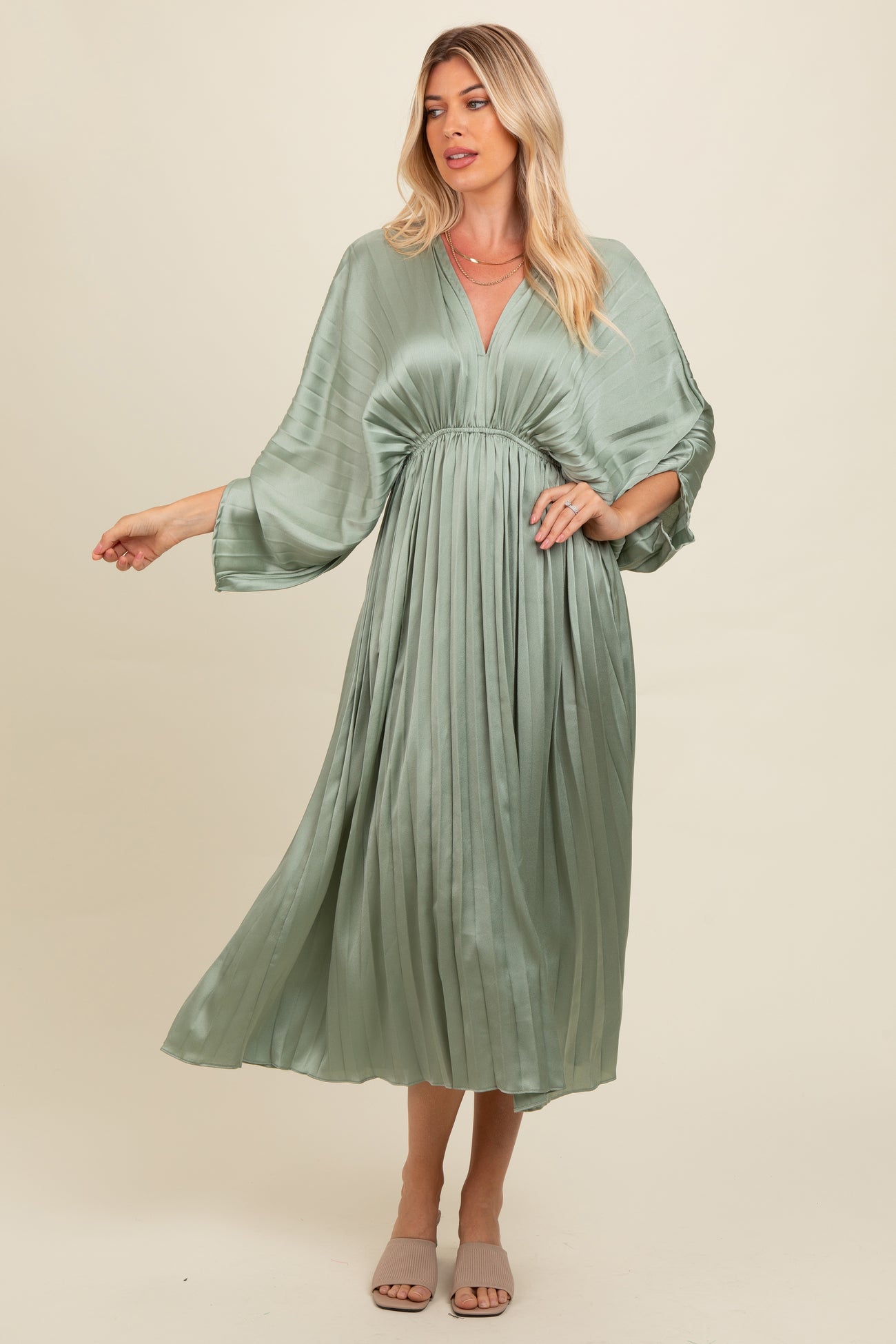 woman wearing a light green pleated maxi dress with a deep v-neck and wide sleeves