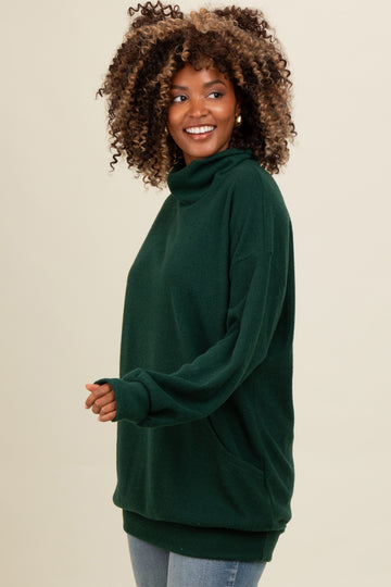 woman wearing a dark green cowl neck pullover sweater with side pockets and relaxed fit, styled with light blue jeans