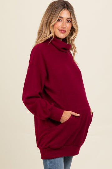 woman wearing a burgundy oversized turtleneck maternity sweatshirt with pockets and a visible baby bump