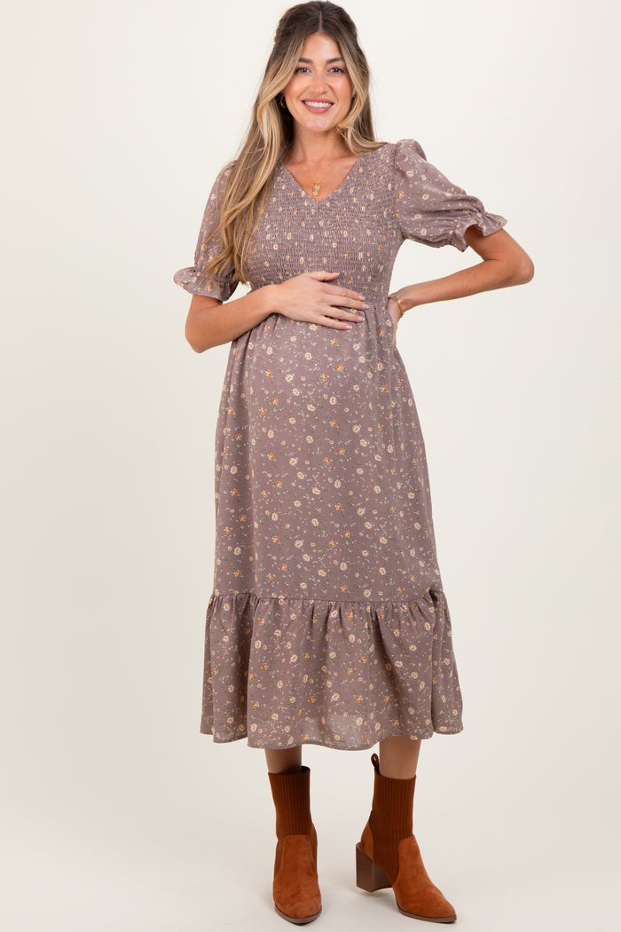 woman wearing a brown floral maternity dress with puff sleeves and a ruffled hem, holding her baby bump