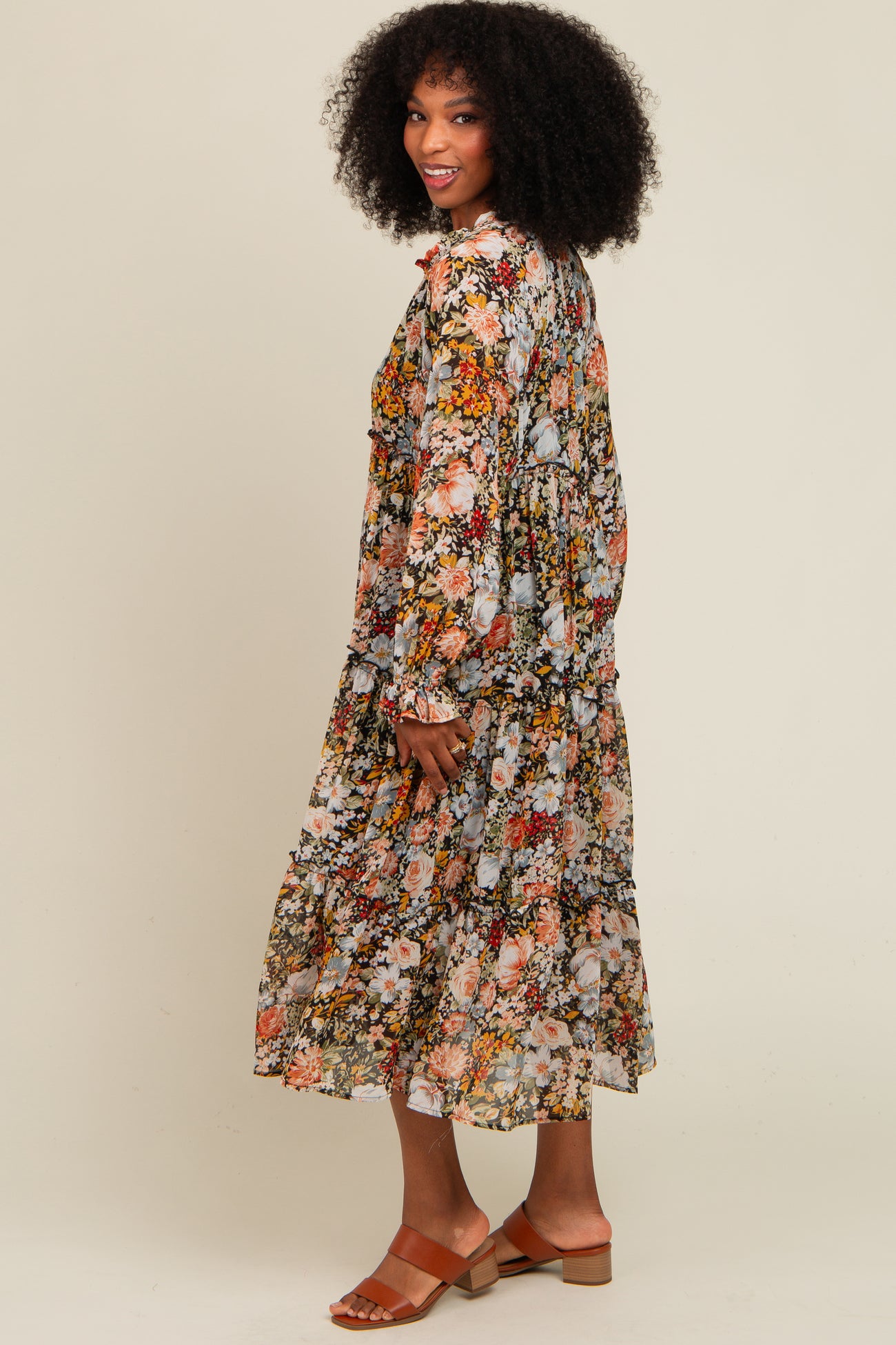 woman wearing a long floral print dress with tiered ruffles and bell sleeves, standing and smiling sideways