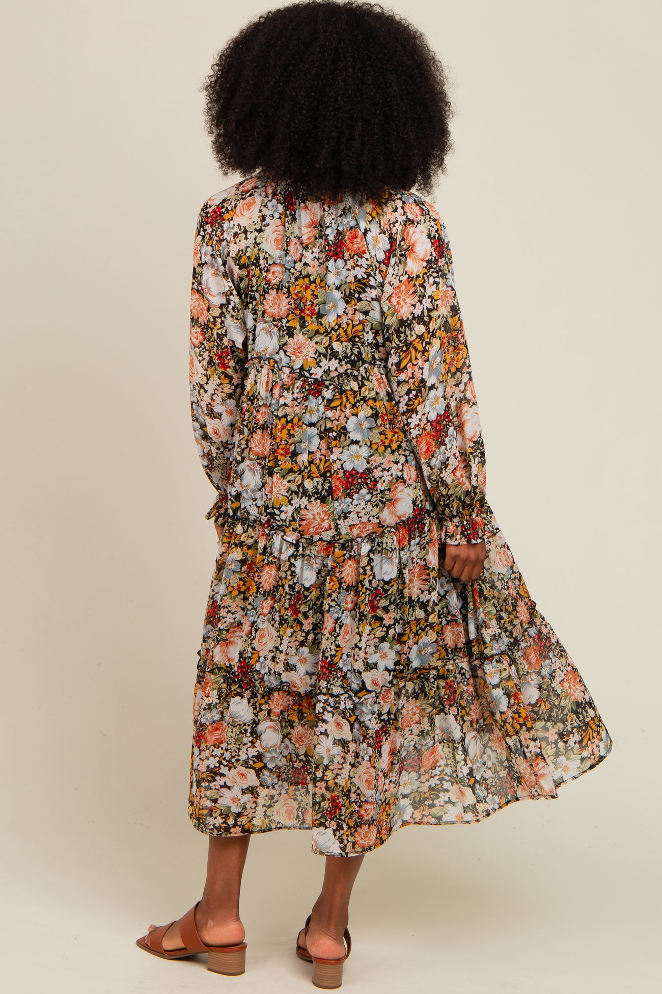 woman wearing a floral long sleeve maxi dress with a tiered skirt, standing with her back to the camera