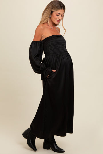 woman wearing a black off-the-shoulder maternity dress with long sleeves and a smocked bodice, showing her baby bump
